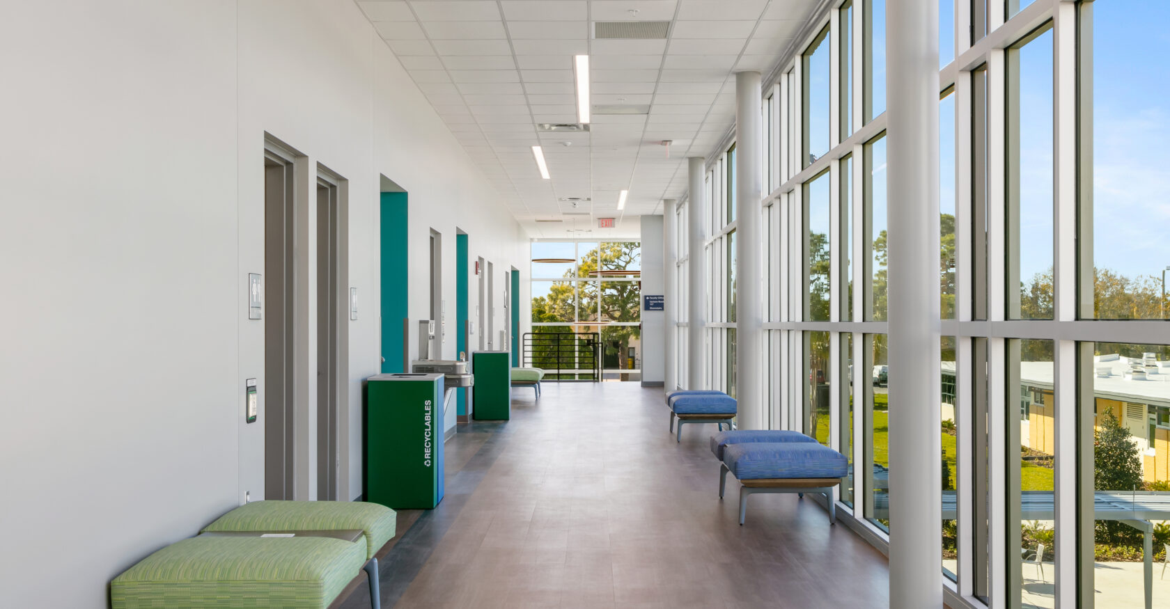SCF Science building hallway with large floor to ceiling windows letting in a lot of light with blue and green seating for students